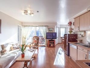 A spacious living room with a sofa, a coffee table, and a TV. There is a kitchen area with cabinets and a refrigerator. - Apartment Le Hoc by Interhome (Deauville-Trouville)