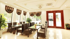 A spacious room with a dining area featuring a glass table and wicker chairs, large windows with decorative curtains, and a red door leading outside. - Diamond Hotel (Ninh Binh)