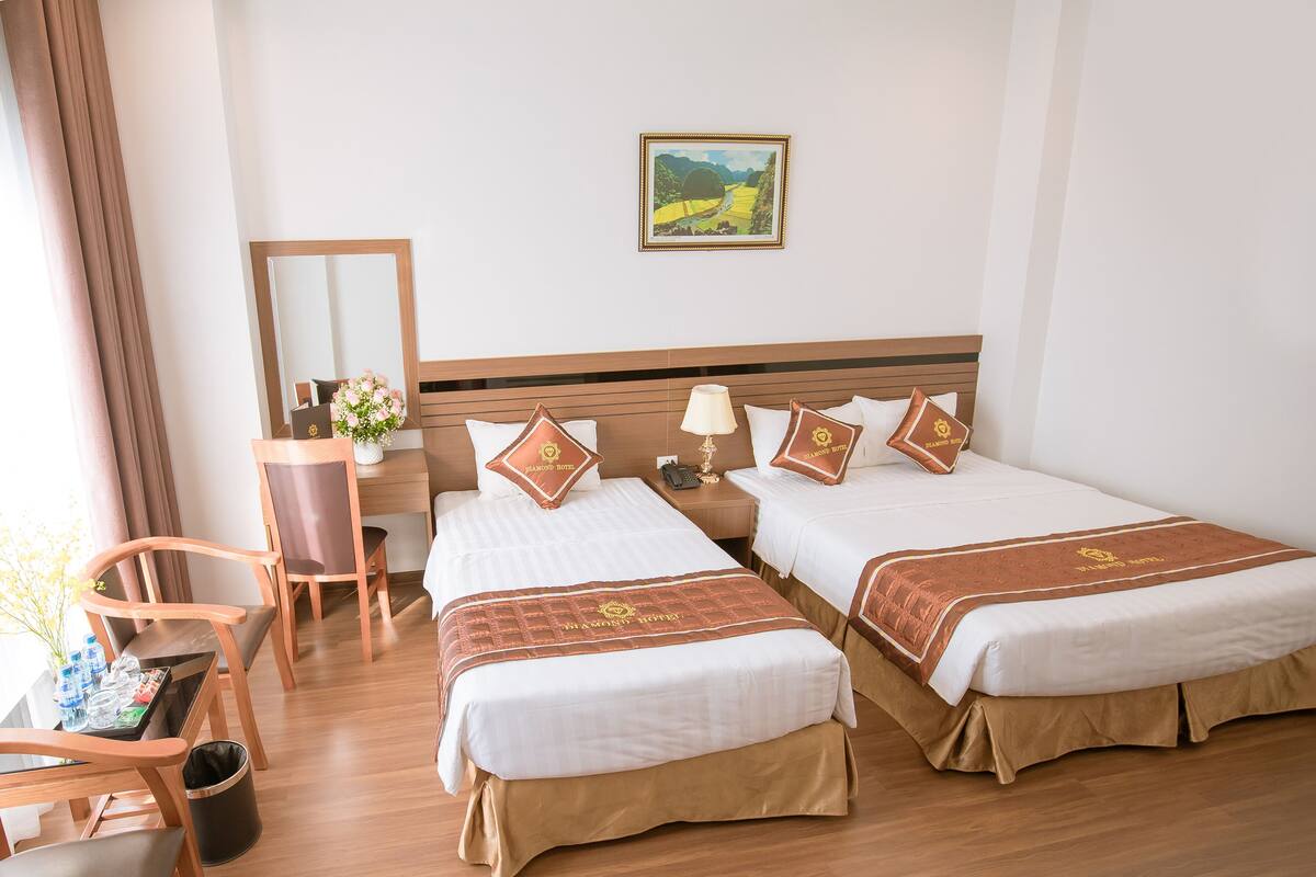 A hotel room with two beds, a desk, a chair, and a mirror.