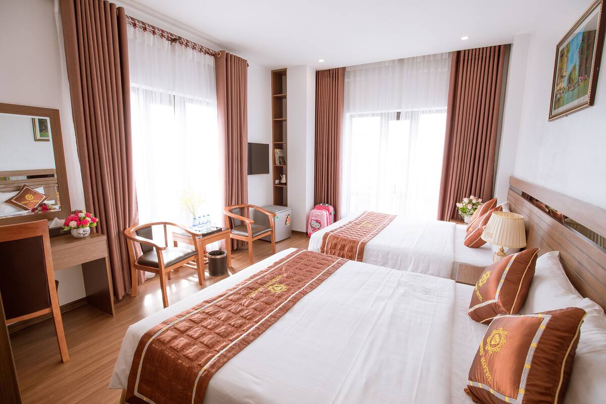 A hotel room with two beds, a desk, a chair, a TV, and a bookshelf.