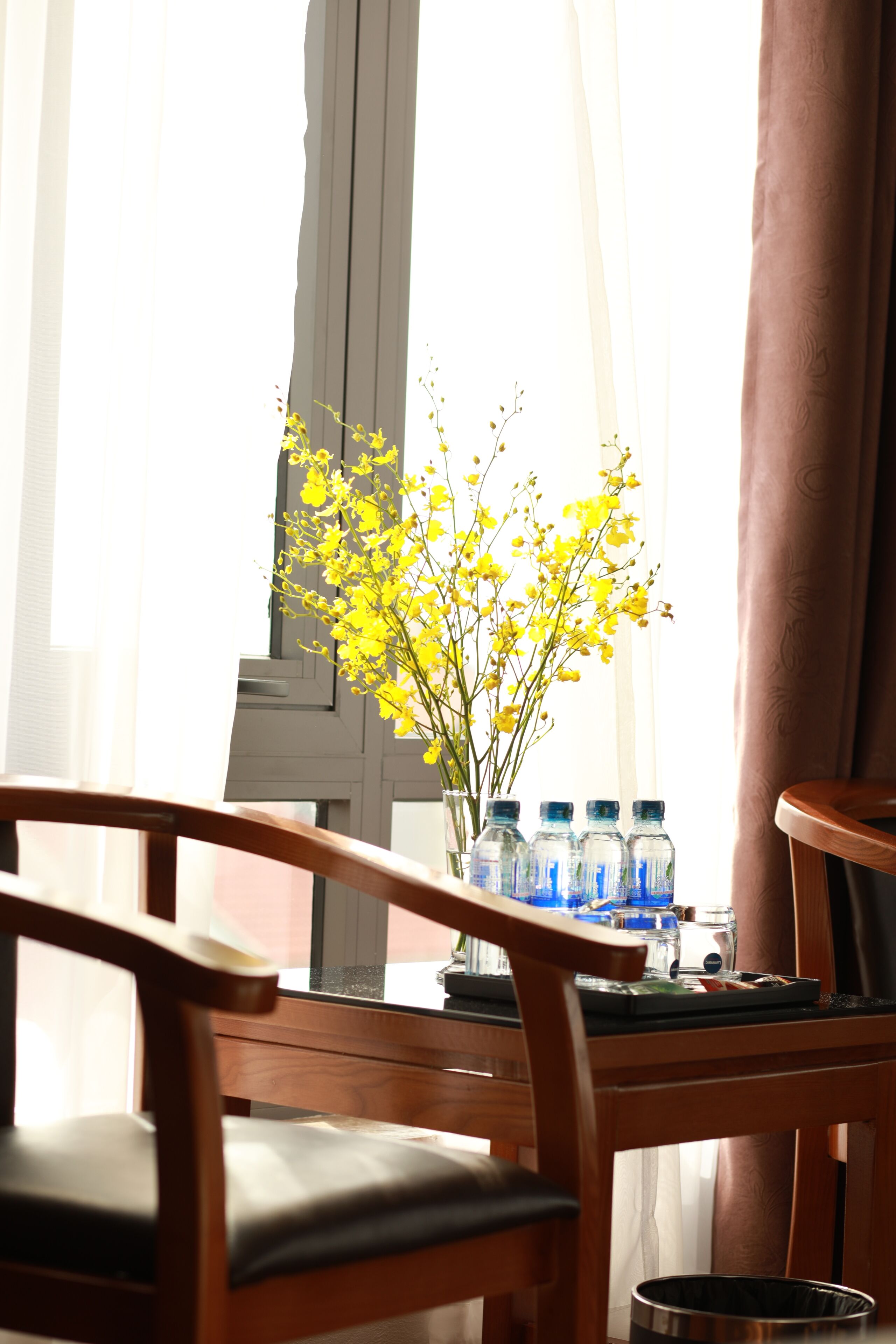 A wooden table with a vase of yellow flowers and several water bottles.