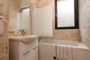 Ein Badezimmer mit Badewanne, Waschbecken und einem Fenster mit Jalousien.