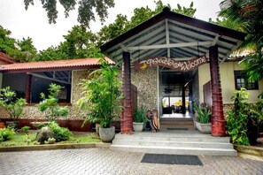 A building with a covered entrance, a stone wall, and potted plants. - Happy Banana Hotel & Restaurant (Unawatuna)