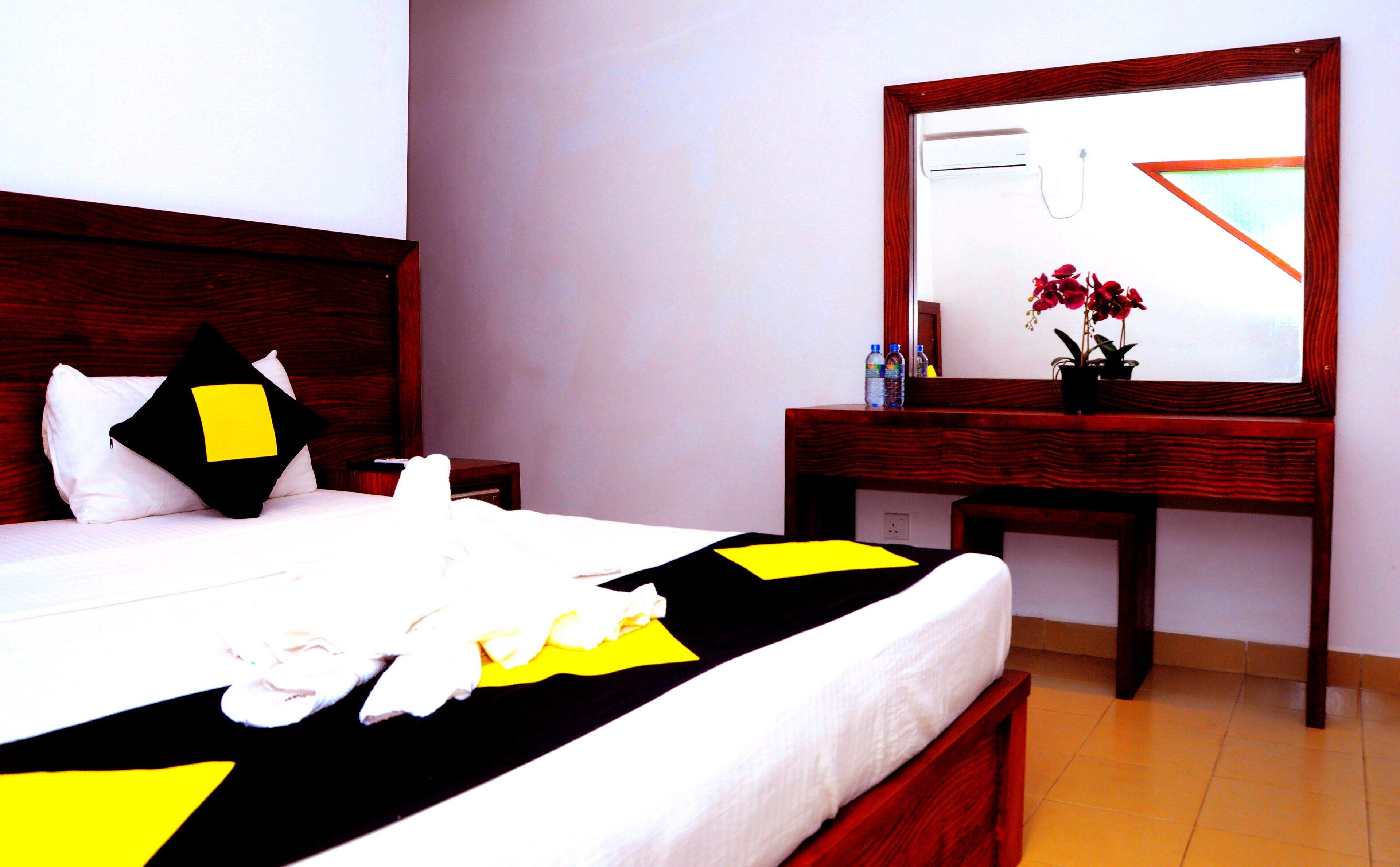 A neatly made bed with a black and yellow bedspread, a wooden headboard, and a bedside table with a mirror.
