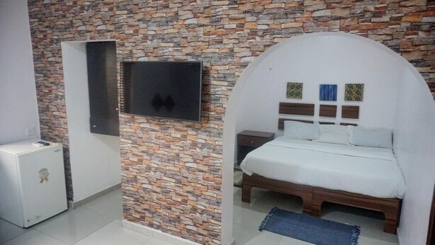 Ein Schlafzimmer mit Steinwand, einem Bett mit weißem Kopfteil, einem an der Wand montierten Fernseher und einem kleinen Nachttisch.