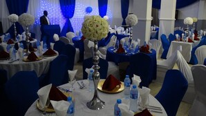 Ein Bankettsaal mit runden Tischen, blau-weißer Vorhangdekoration und floralen Tischgestecken.