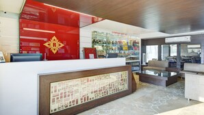A hotel reception area with a red and white color scheme, a glass display case with various items, and a seating area with sofas. - Raya Inn (Jaipur)