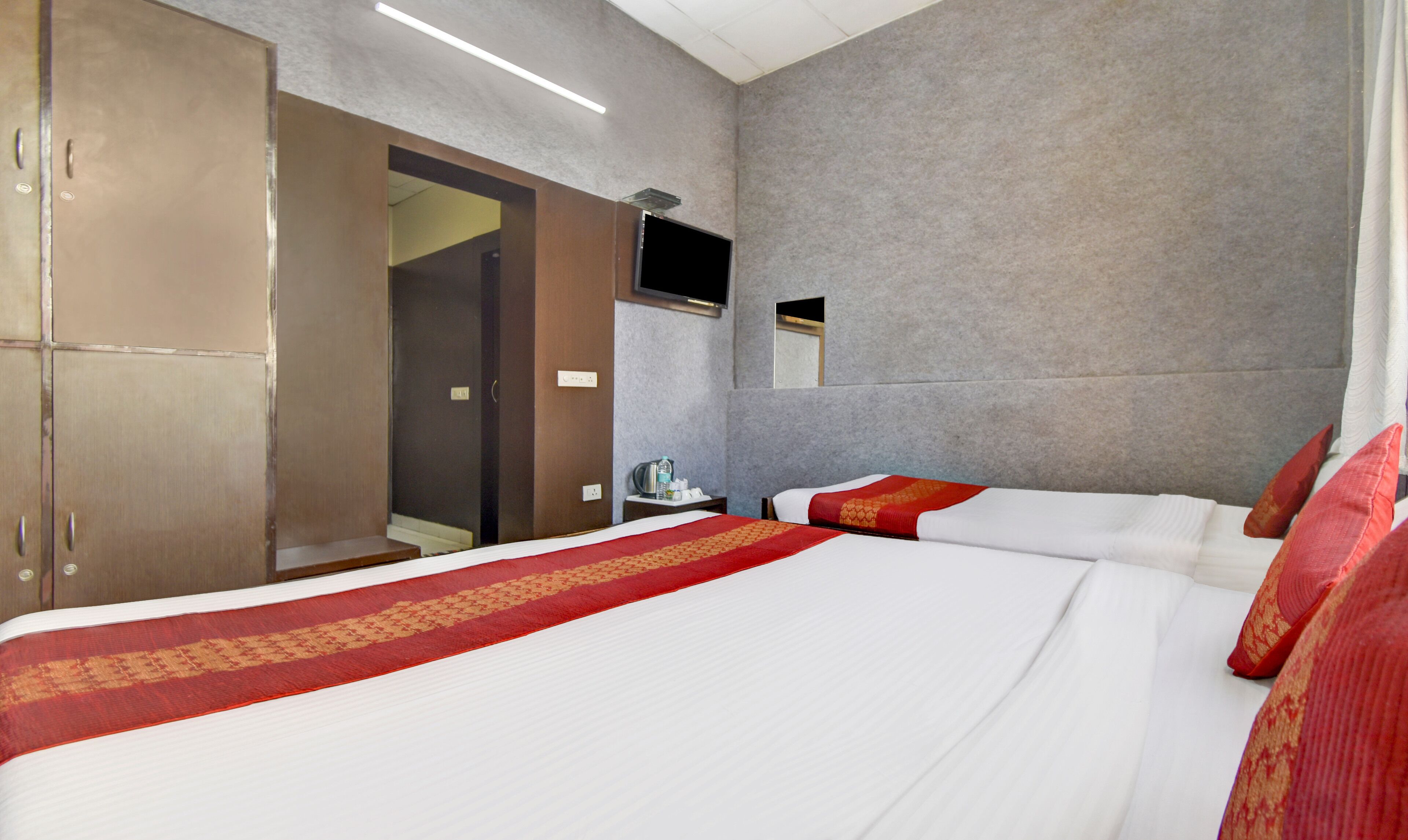 A hotel room with a large bed, a wardrobe, a television mounted on the wall, and a small table with a water bottle.