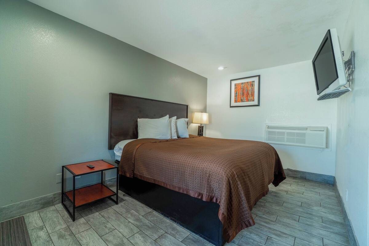 A hotel room with a bed, a nightstand, a TV mounted on the wall, and a painting.