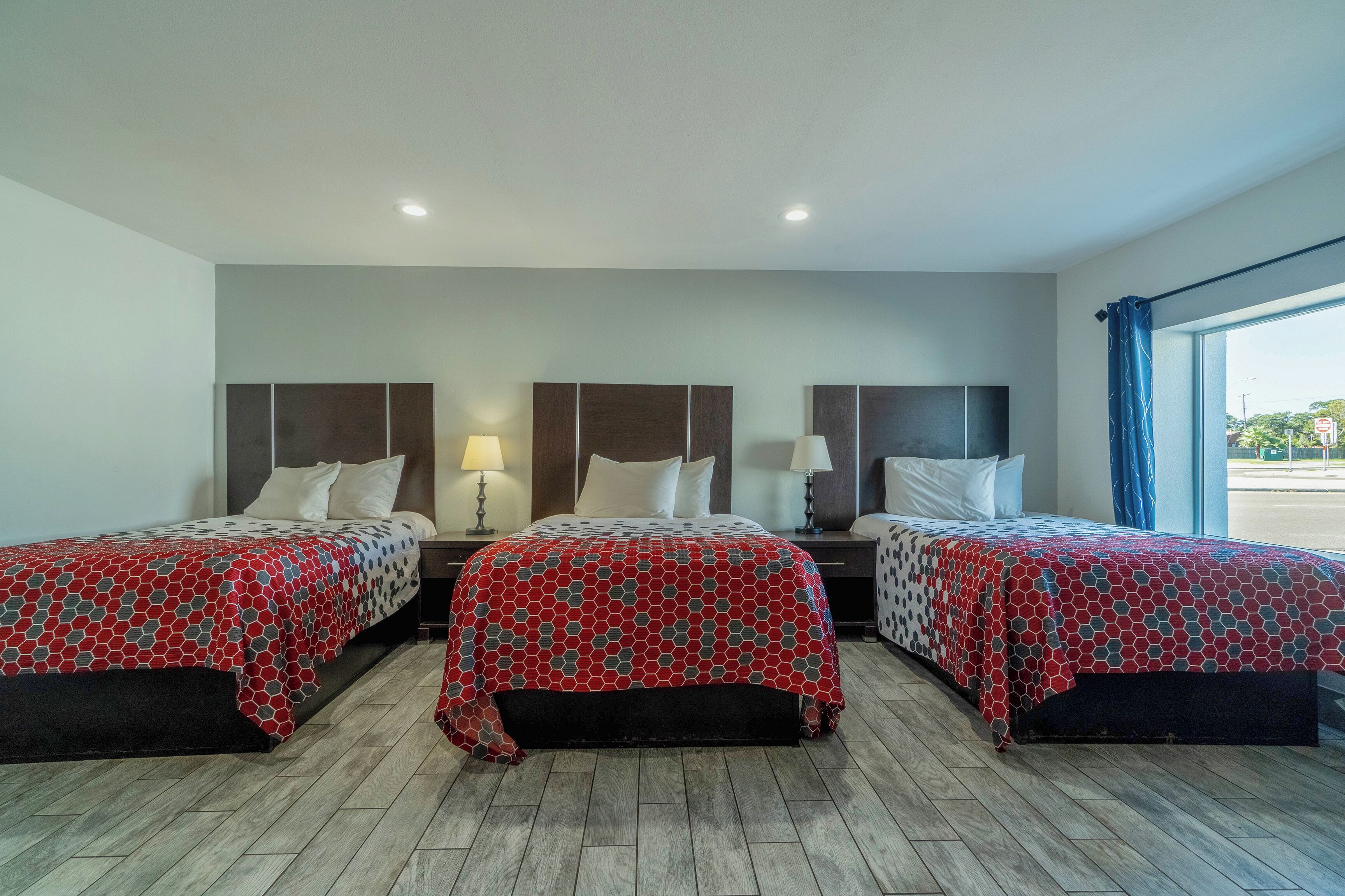 A hotel room with three beds, each with a patterned bedspread, wooden headboards, and bedside lamps.