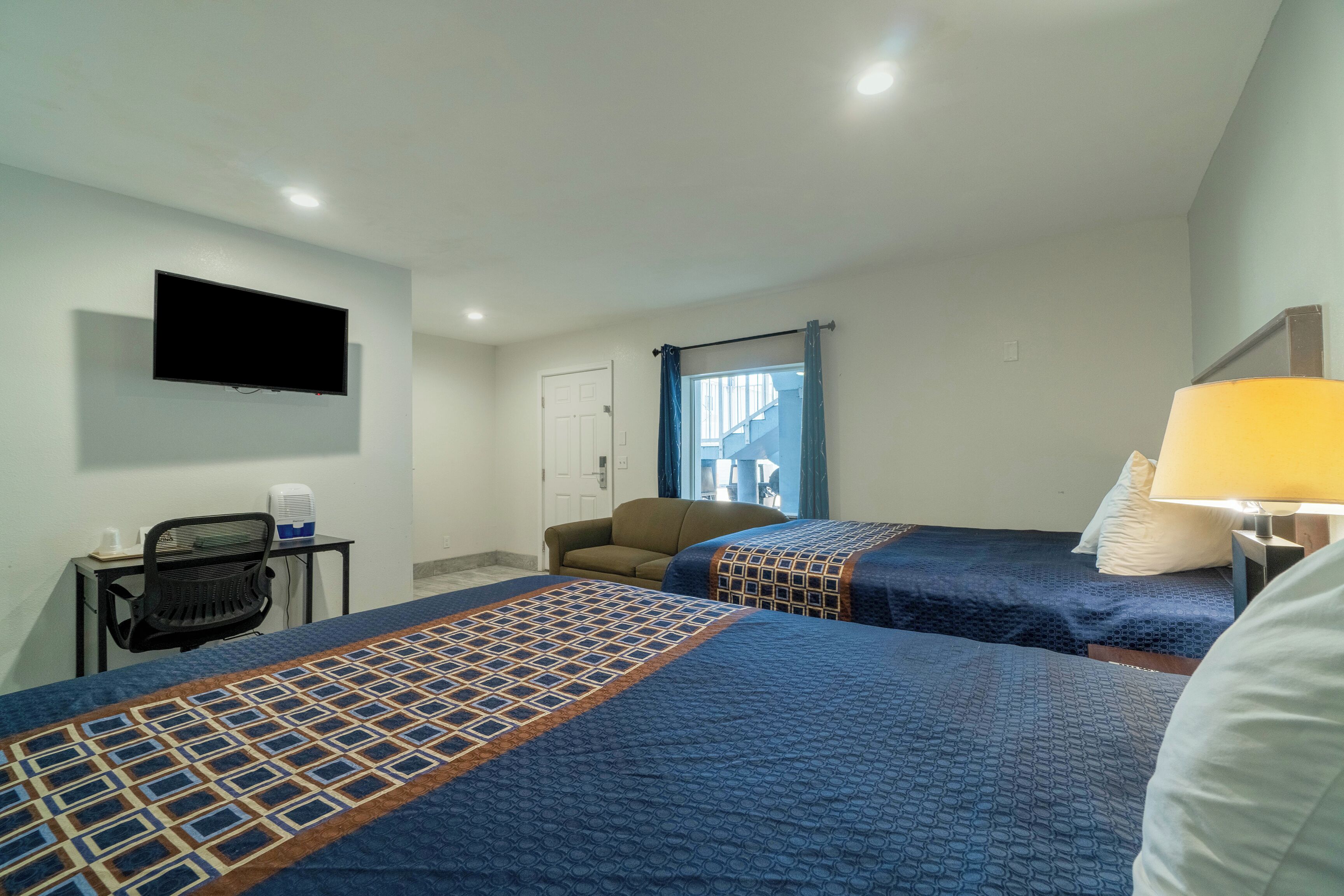 Een hotelkamer met twee bedden, een bureau met stoel, een aan de muur bevestigde televisie en een raam met gordijnen.