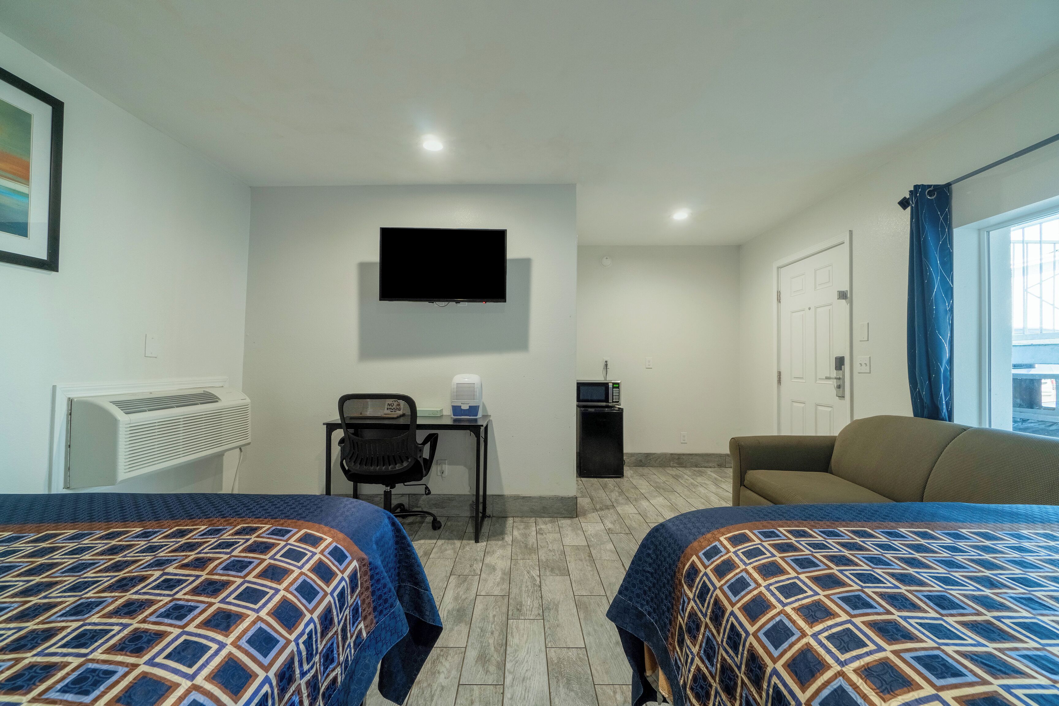 A hotel room with two beds, a desk with a computer, a TV, and a window with curtains.