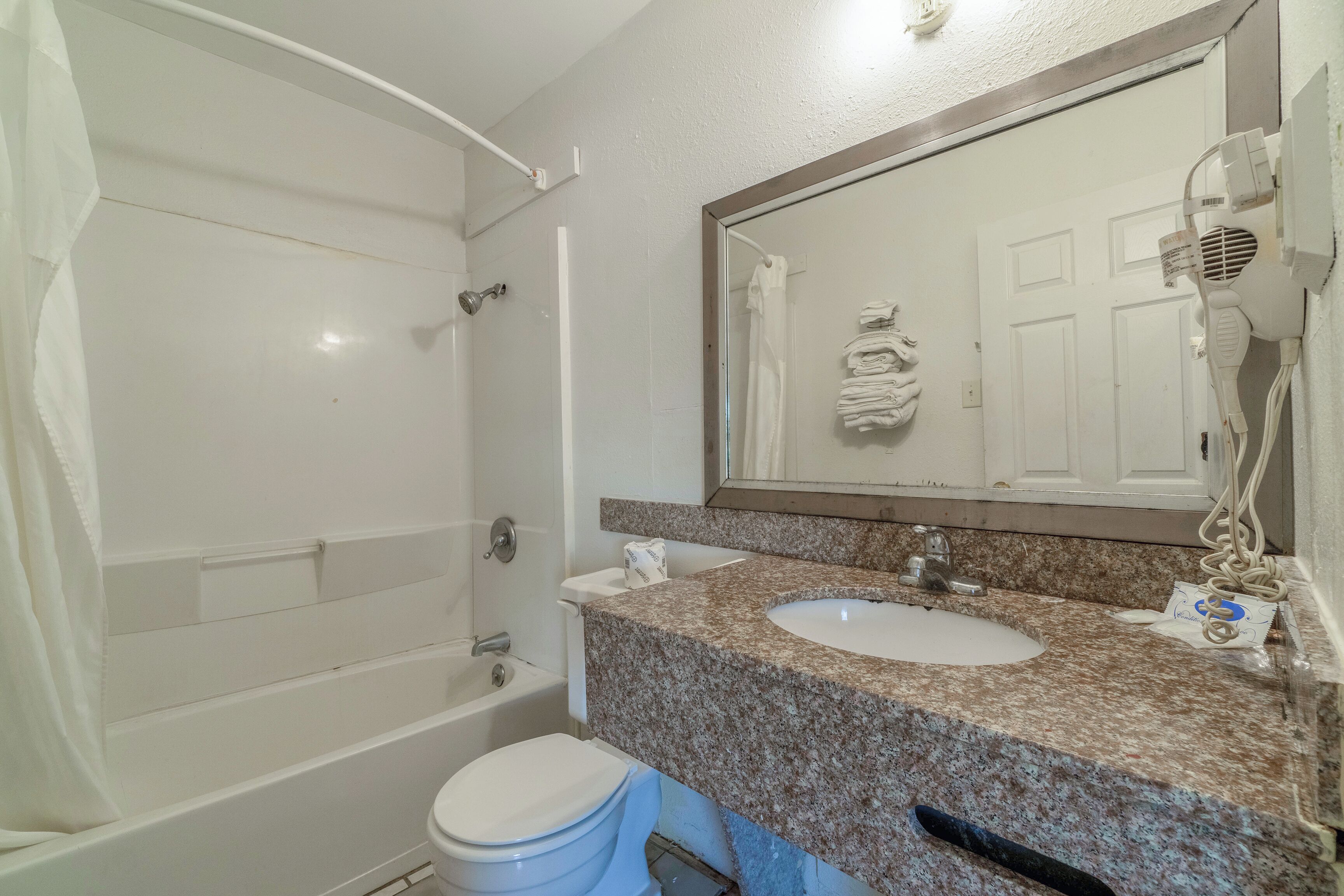 A bathroom with a white bathtub, a sink with a granite countertop, and a large mirror above the sink.