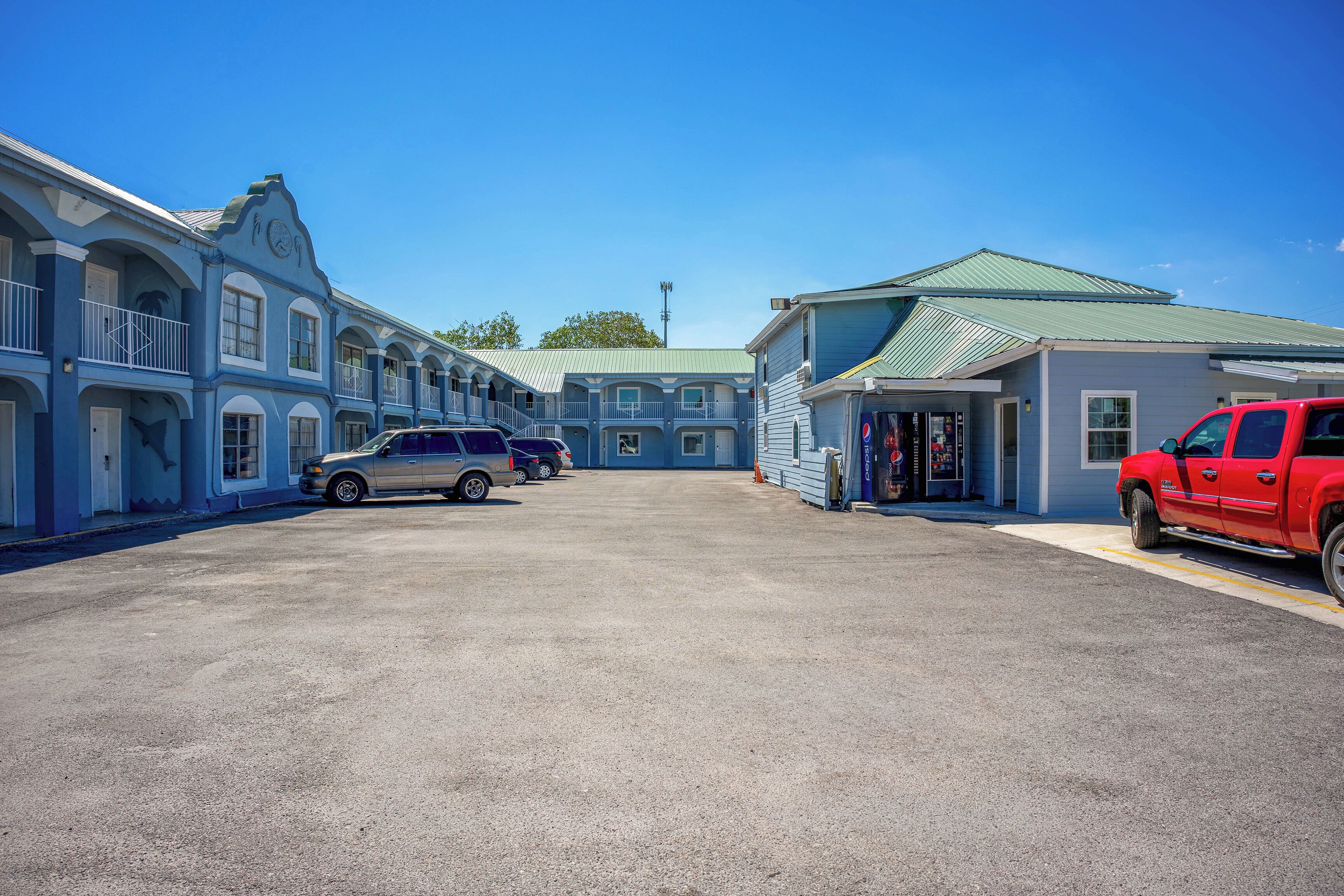 A motel with a central parking area, a red truck, and a silver SUV.