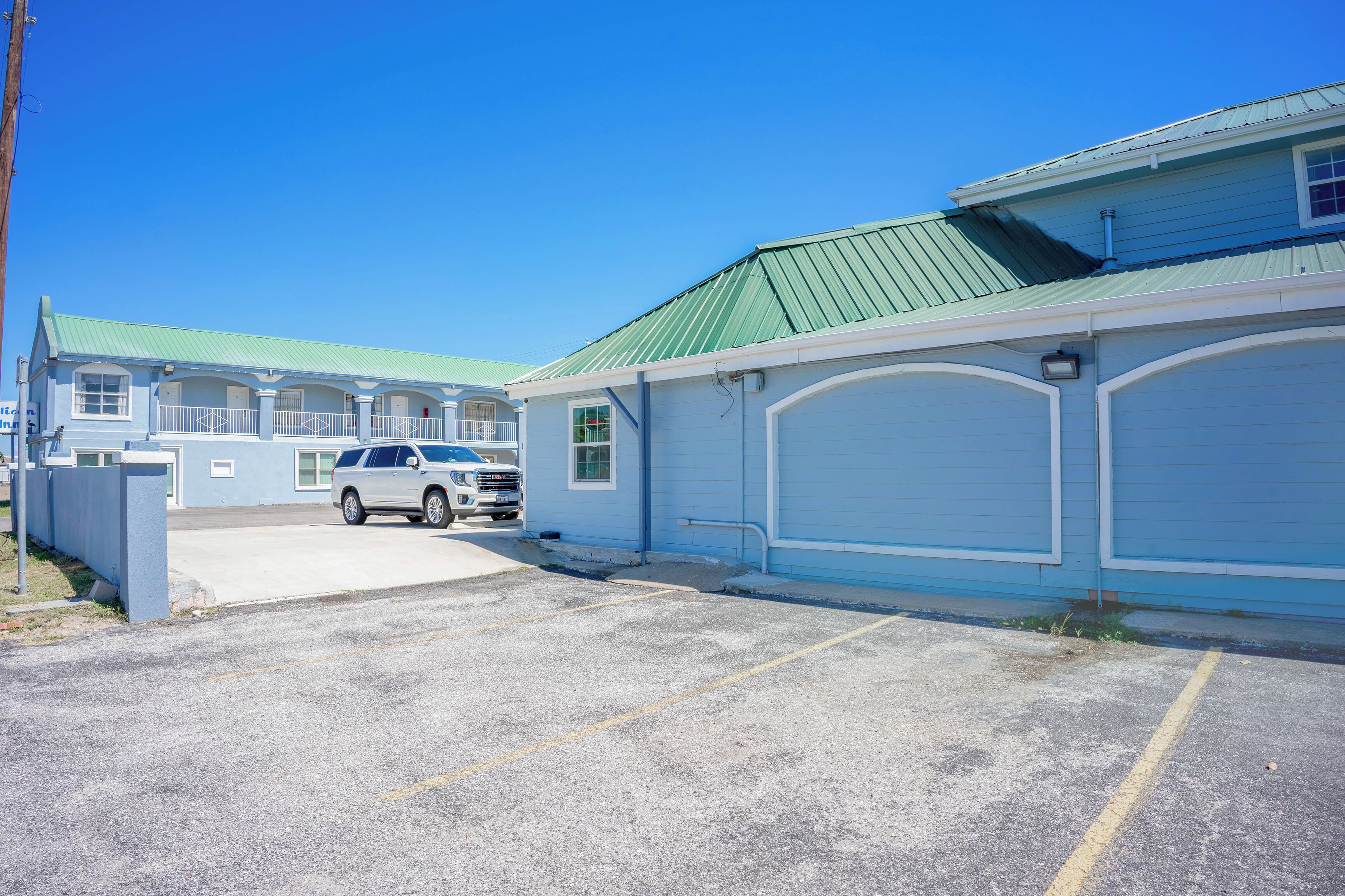 A motel with a parking lot, a white SUV parked in front, and a building with a green roof.