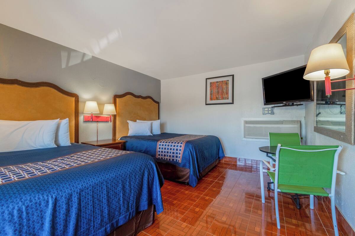 A hotel room with two beds, a TV, a table with chairs, and a window.