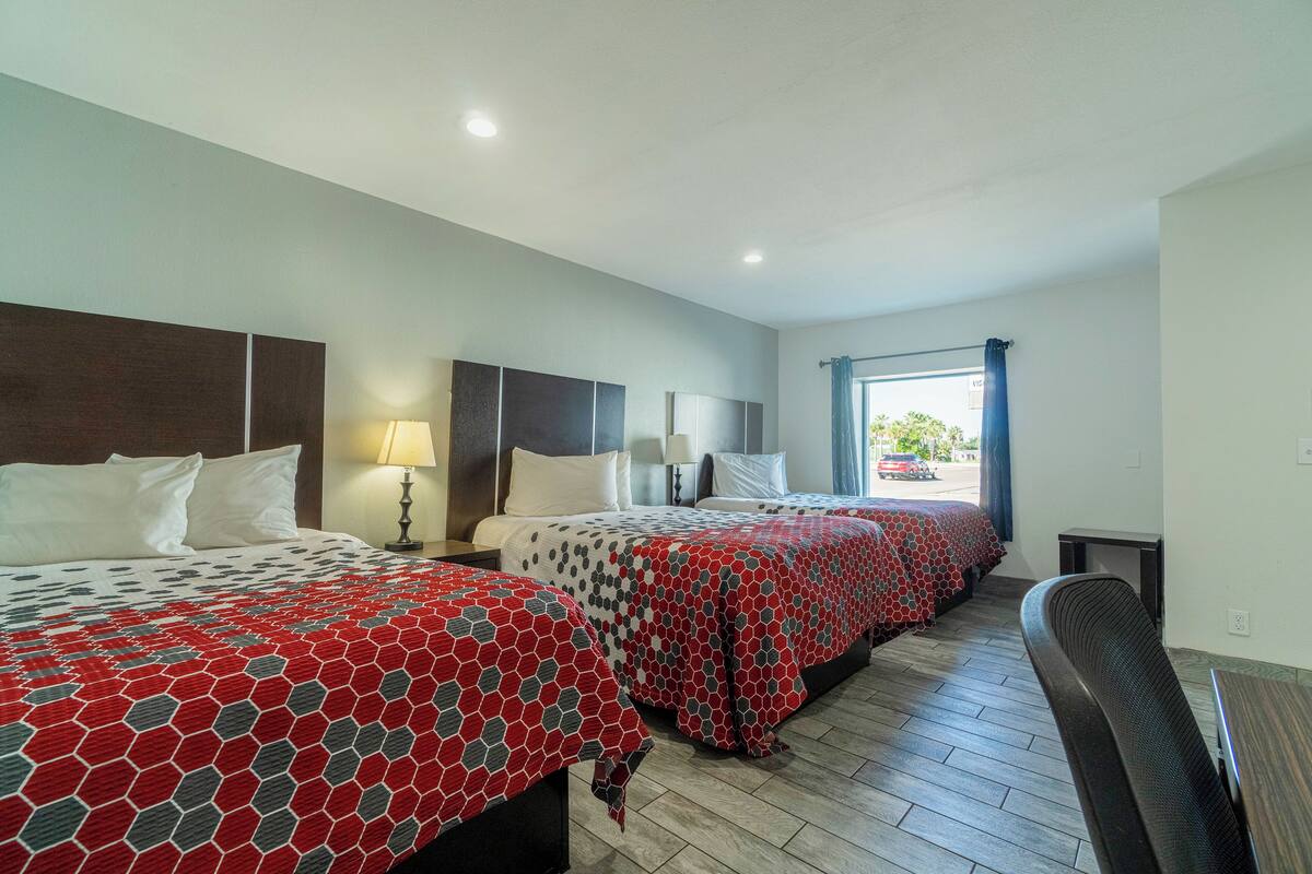 A hotel room with two beds, a desk, and a window with curtains.