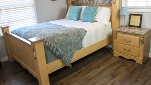 A wooden bed with a headboard, two pillows, a bedside table with drawers, and a wall-mounted lamp. - Wonderful 3BDR Guest Suite Sits Between Downtown and the Beach (Charleston)