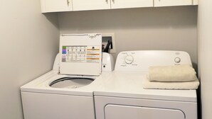 A compact laundry area with a front-loading washing machine and a dryer, a control panel, and a white towel on the dryer. - Wonderful 3BDR Guest Suite Sits Between Downtown and the Beach (Charleston)