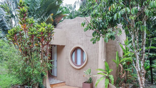 A unique, nature-integrated building with a circular window, surrounded by lush greenery and a gravel pathway. - OYO 742 View Pruksa Resort (Ranong)