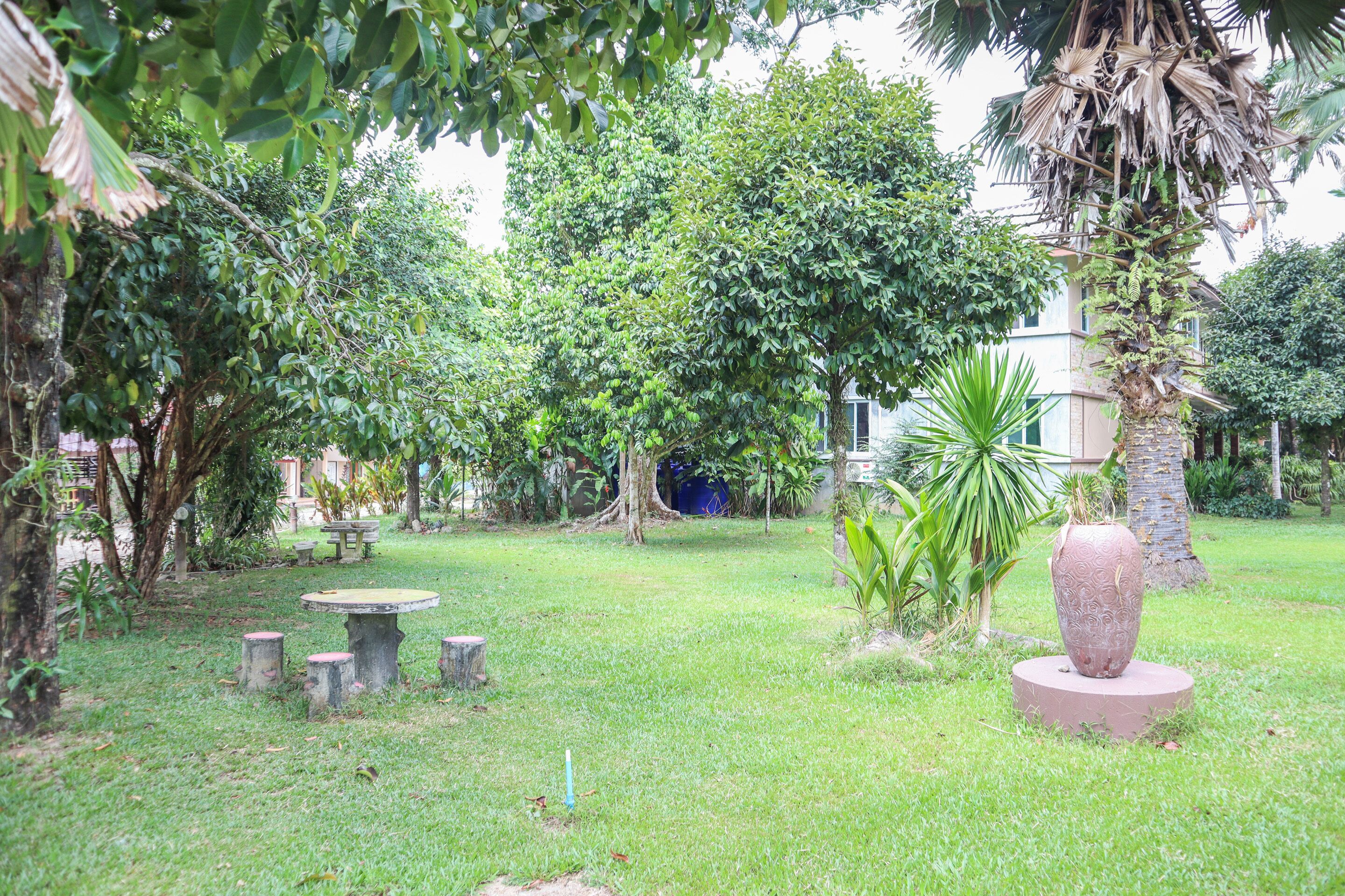 A garden with a stone table and benches, surrounded by lush greenery and a large decorative vase.