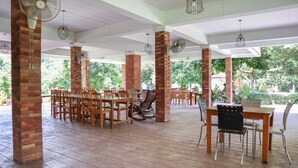 An outdoor patio area with brick pillars, wooden tables and chairs, and ceiling fans. - OYO 742 View Pruksa Resort (Ranong)