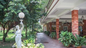 A covered walkway with a statue, potted plants, and a brick building with a clock. - OYO 742 View Pruksa Resort (Ranong)