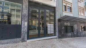 A modern building with large glass windows, a metal awning, and a tiled ground.