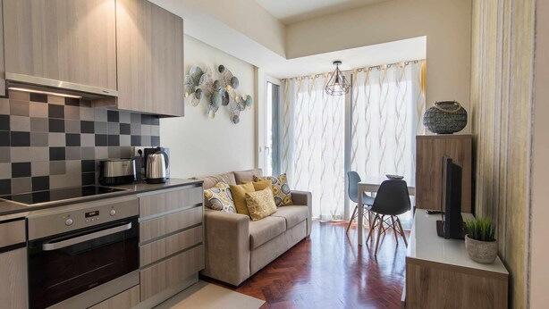 A modern kitchen with a built-in oven, a dining area with a table and chairs, and a living space with a sofa and decorative wall art.
