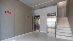 A modern elevator area with a sign indicating an electrical room, a staircase, and a clean, tiled floor.