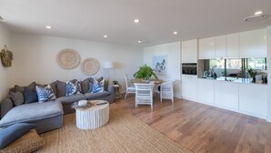 A modern living room with a grey sectional sofa, a round coffee table, and a dining area with white chairs. - Oceanview Kiama Luxury Coastal Accommodation (Kiama)