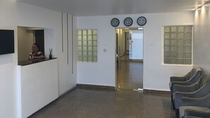 A reception area with a counter, three clocks, a glass door, and a seating area with chairs. - RM Suites (Lagos)