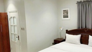 A bedroom with a bed, a nightstand, a wooden wardrobe, and a door. - RM Suites (Lagos)