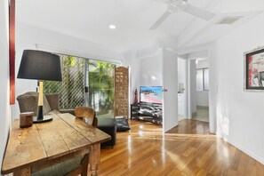 A spacious room with a wooden dining table, a TV, and a view of a beach through a sliding glass door.