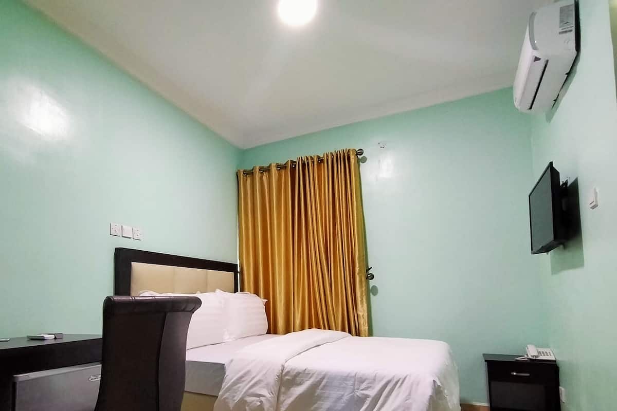 A hotel room with a bed, a desk, a chair, a TV mounted on the wall, and a curtain.