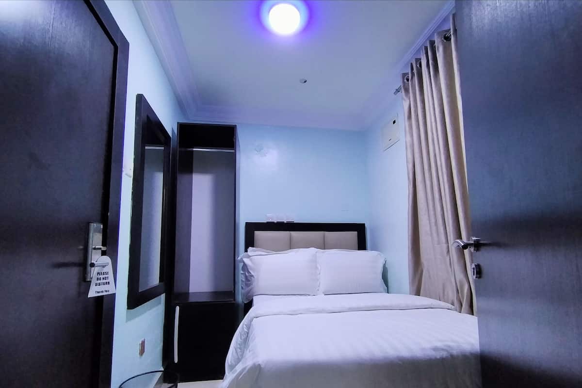 A hotel room with a bed, a nightstand, a mirror, and a door with a 'Please Do Not Disturb' sign.