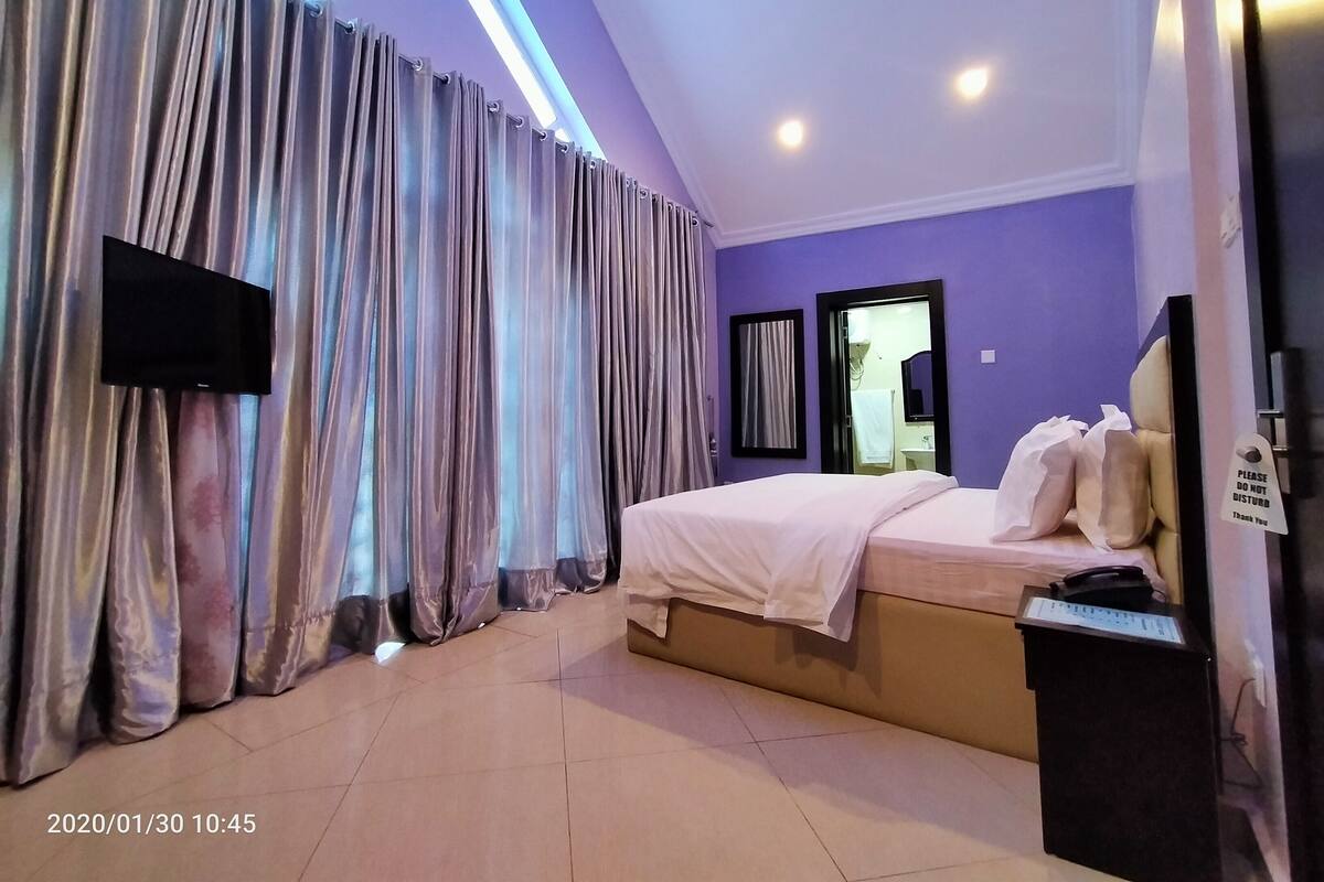 A hotel room with a bed, a television, a mirror, and a sign on the door.