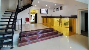 A reception area with a marble staircase, a reception desk, and a TV mounted on the wall. - Beckett Suites (Abuja)