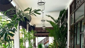 A spacious indoor area with a round table and chairs, surrounded by potted plants and wooden furniture. - The Postcard Galle (Galle)