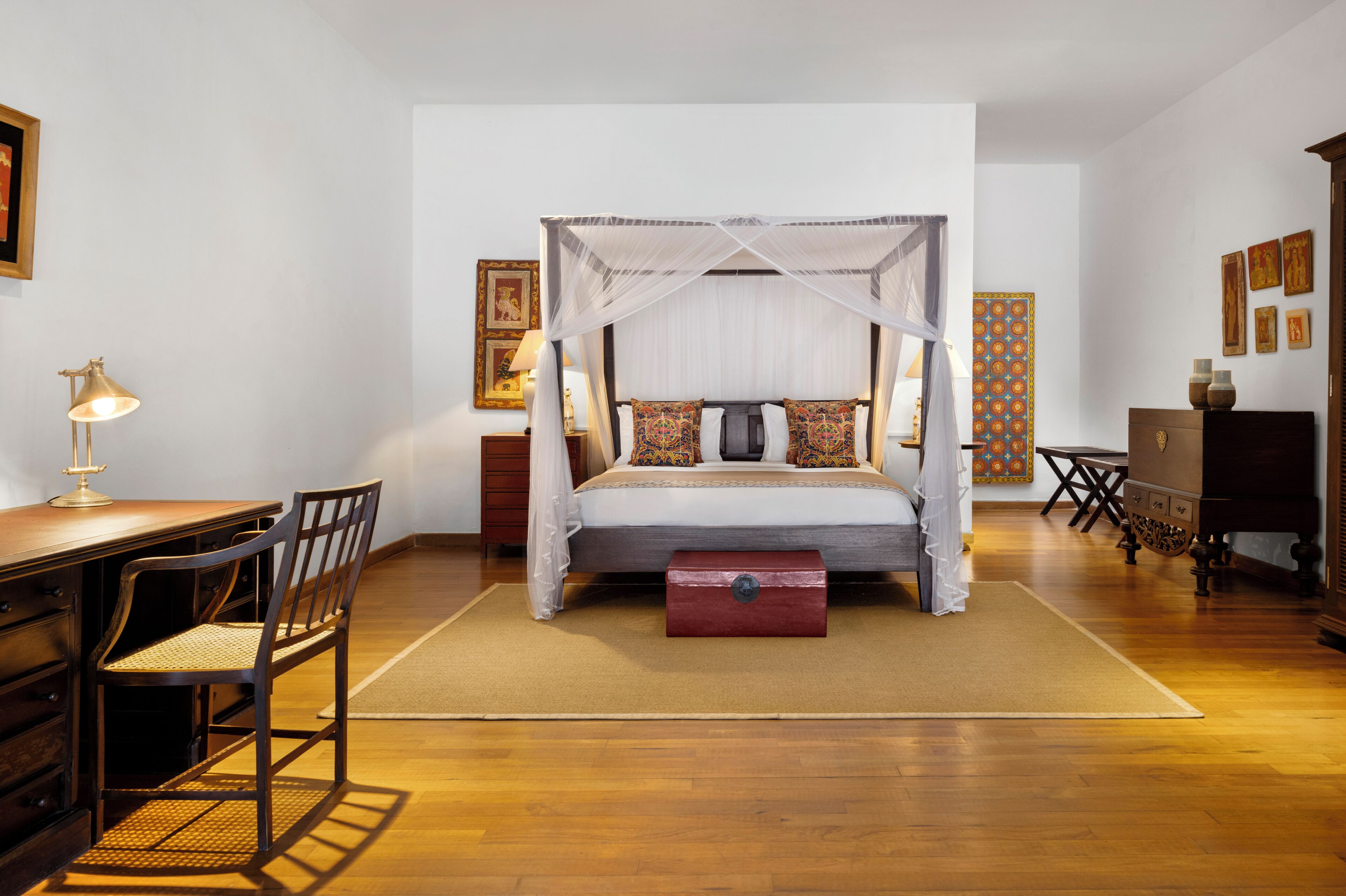 A bedroom with a four-poster bed, a desk with a chair, a dresser, and a nightstand.
