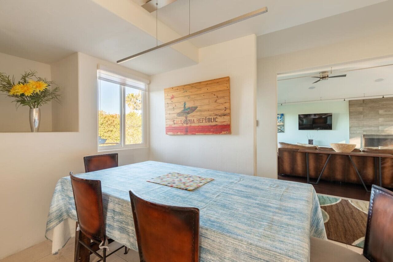 A dining area with a table set for four, a wooden wall art piece, and a view into the kitchen.