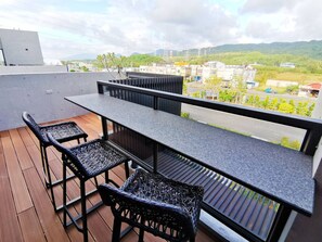 A balcony with a long table and four wicker chairs, overlooking a residential area with buildings and greenery. - Gala Villa (Hengchun)