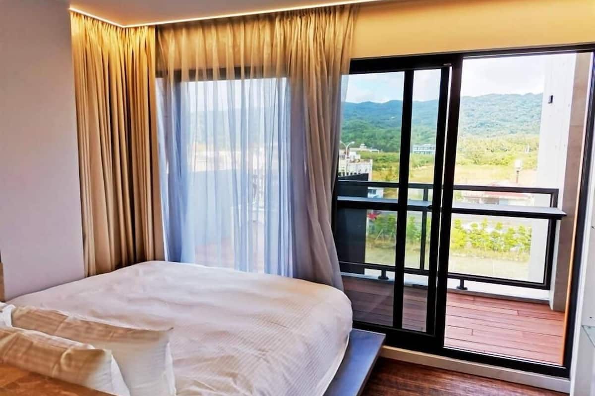 A bedroom with a bed, a view through a large window, and a balcony.