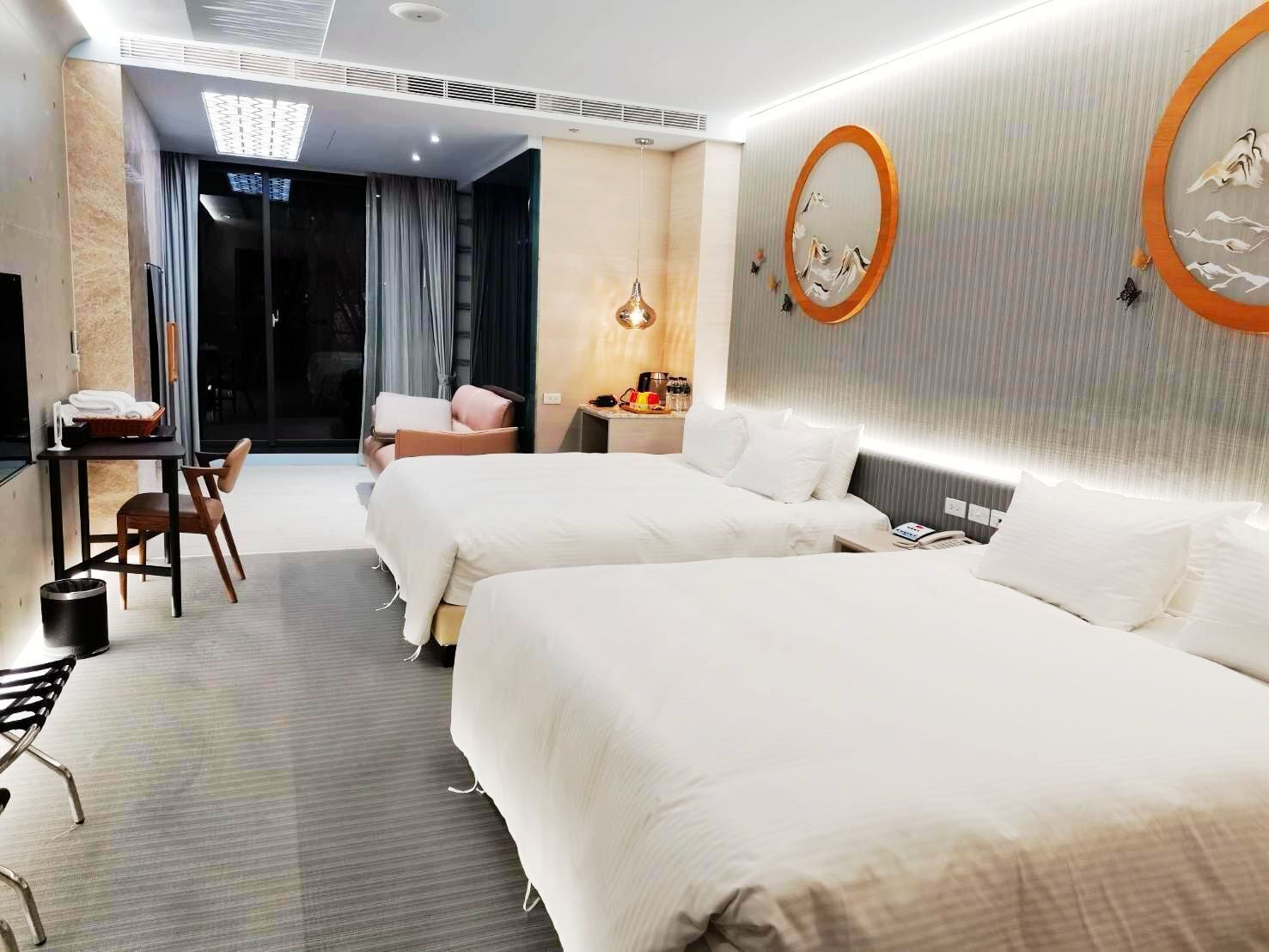 Habitación de hotel con dos camas, un escritorio, una silla, una mesita con artículos de aseo y un espejo instalado en la pared.