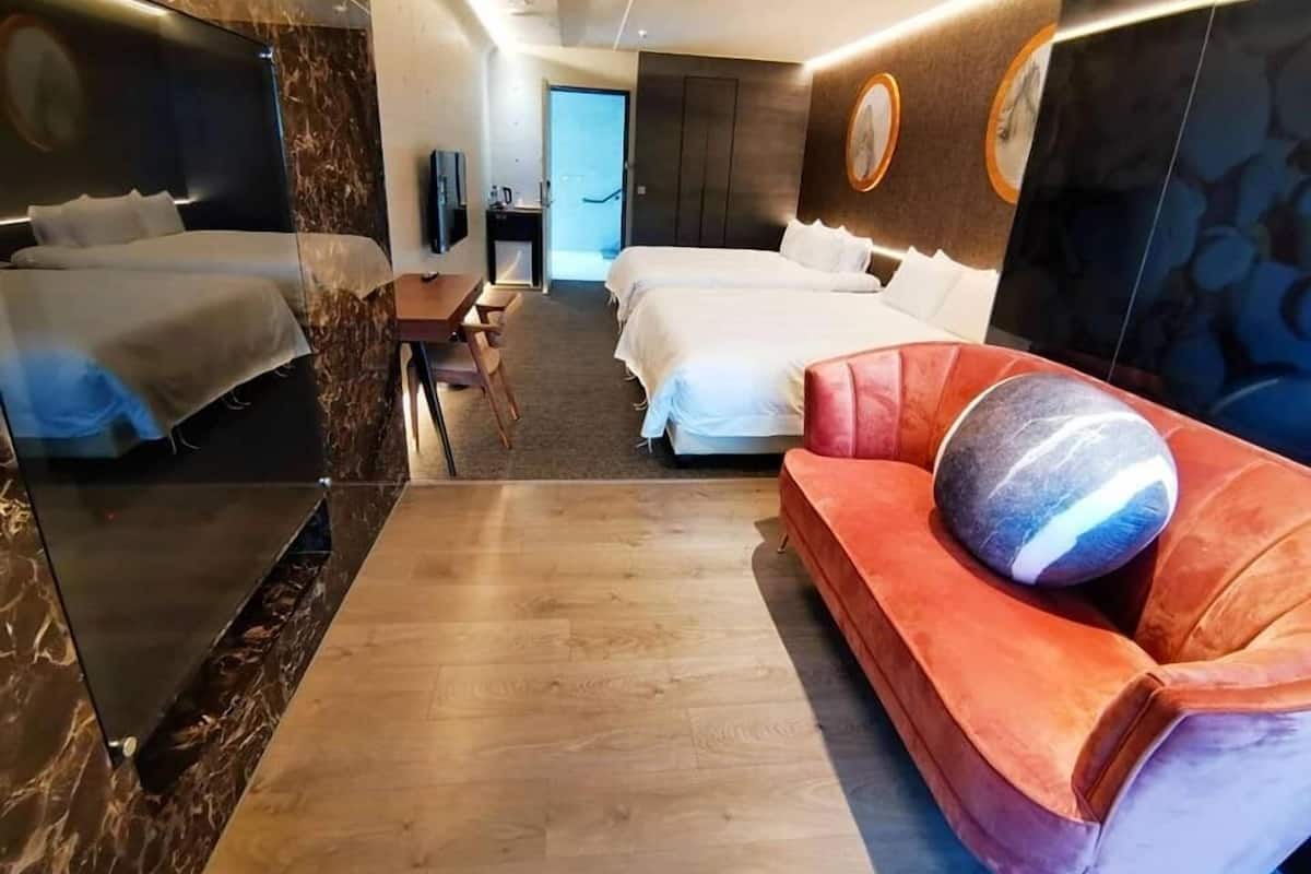 A modern hotel room with two beds, a sofa, a TV, and a desk.
