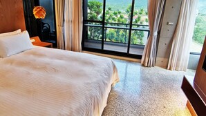 A hotel room with a large bed, a desk, and a view of greenery through a large window. - Gala Villa (Hengchun)