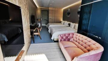 Une chambre d’hôtel moderne équipée d’un grand lit, d’un lit plus petit, d’un canapé, d’un bureau avec une chaise et d’une télévision.