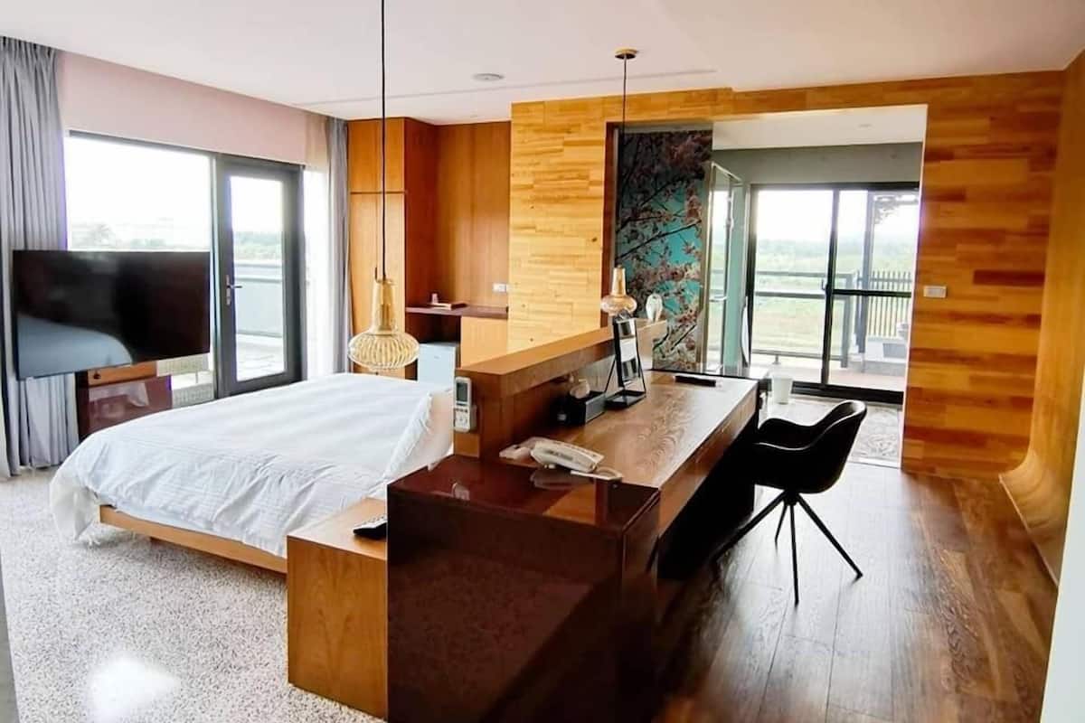 A modern hotel room with a bed, desk, and chair, large windows, and a view of the outdoors.