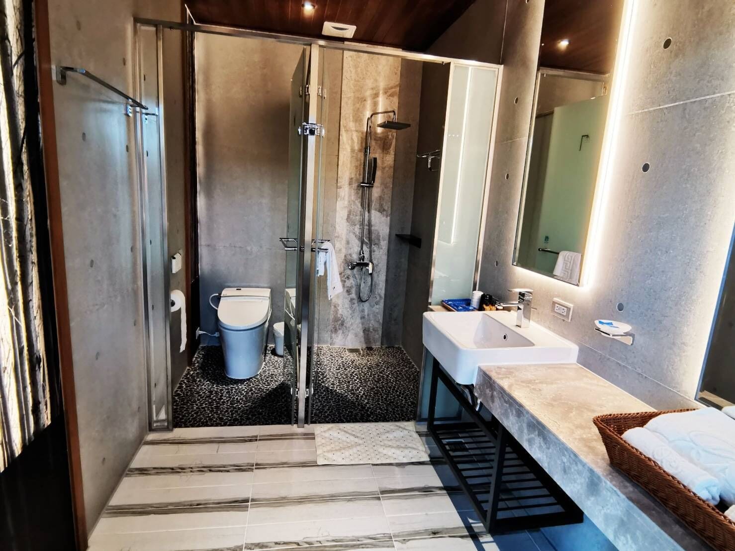 Ein modernes Badezimmer mit Duschkabine aus Glas, Toilette, Waschbecken und großem Spiegel.