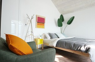A bedroom with a bed, a green sofa, a yellow side table, and a large green plant.